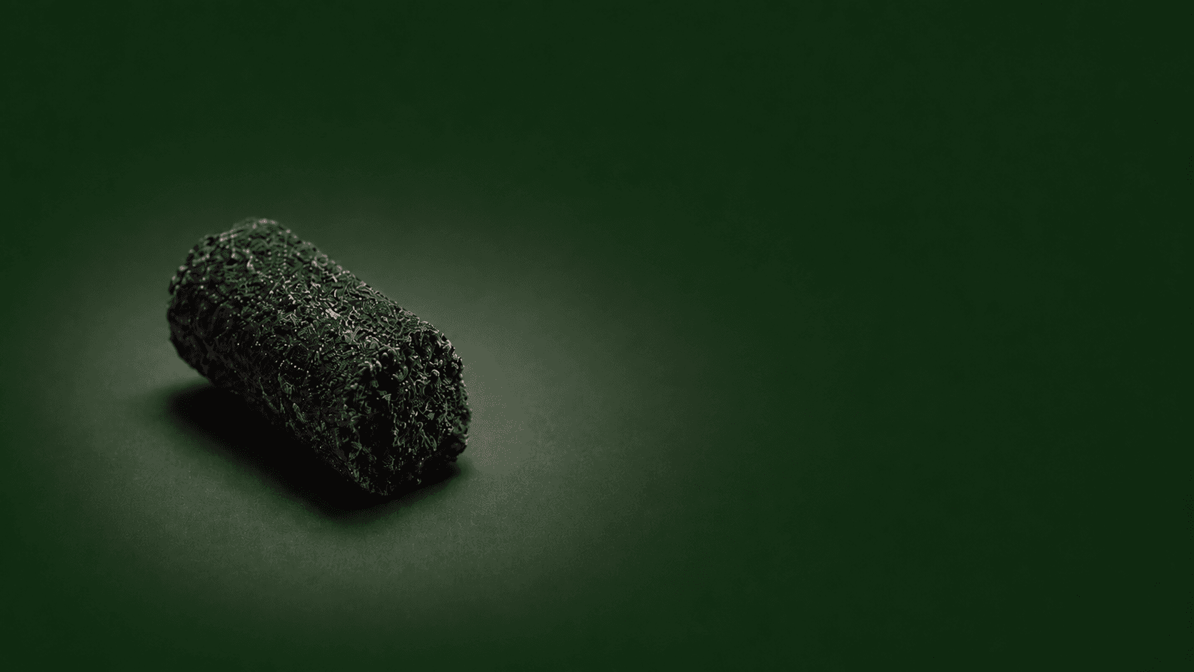 Conceptual close-up of a single dark Reform-style fertilizer pellet positioned to the left on a deep green background.